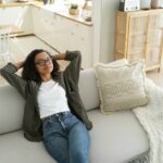 Calm african american girl enjoy fresh conditioned air, resting, sitting on cozy sofa in living room